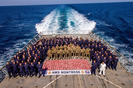 Dozens of Royal Marines and sailors stand around red bags of confiscated drugs on the deck of HMS Montrose