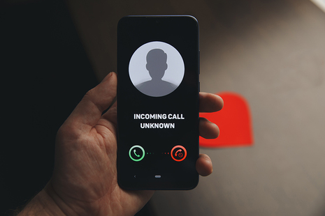 Hand holding a mobile phone. Onscreen an incoming call from an unknown number.