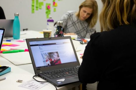 Two people sit at a laptop surrounded by post-it notes during a user research session.
