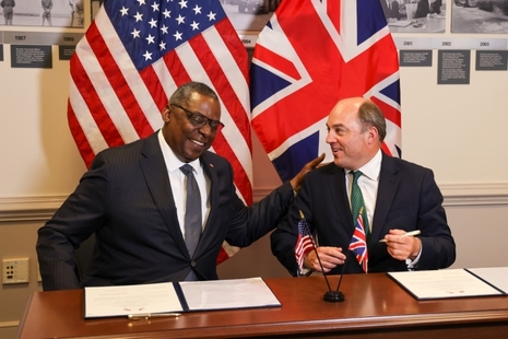 Ben Wallce and Lloyd Austin smile as they sign the agreement extension in front of the UK and US flags