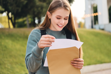 Female student opens envelope with results letter inside.