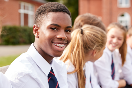 Male student smiles while sat with classmates.