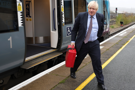 Boris Johnson carrying a red box walking next to a train.