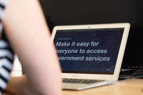Person sits at a laptop which shows a slide saying "Our mission: to make it easier for everyone to access government services".