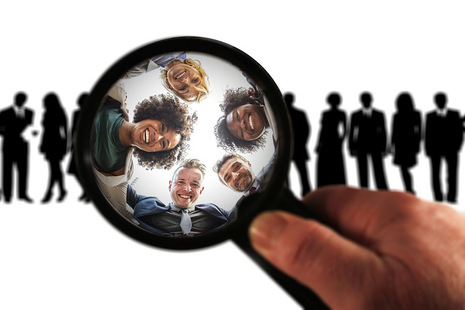 Magnifying glass focusing on 5 faces from a larger group of people in silhouette