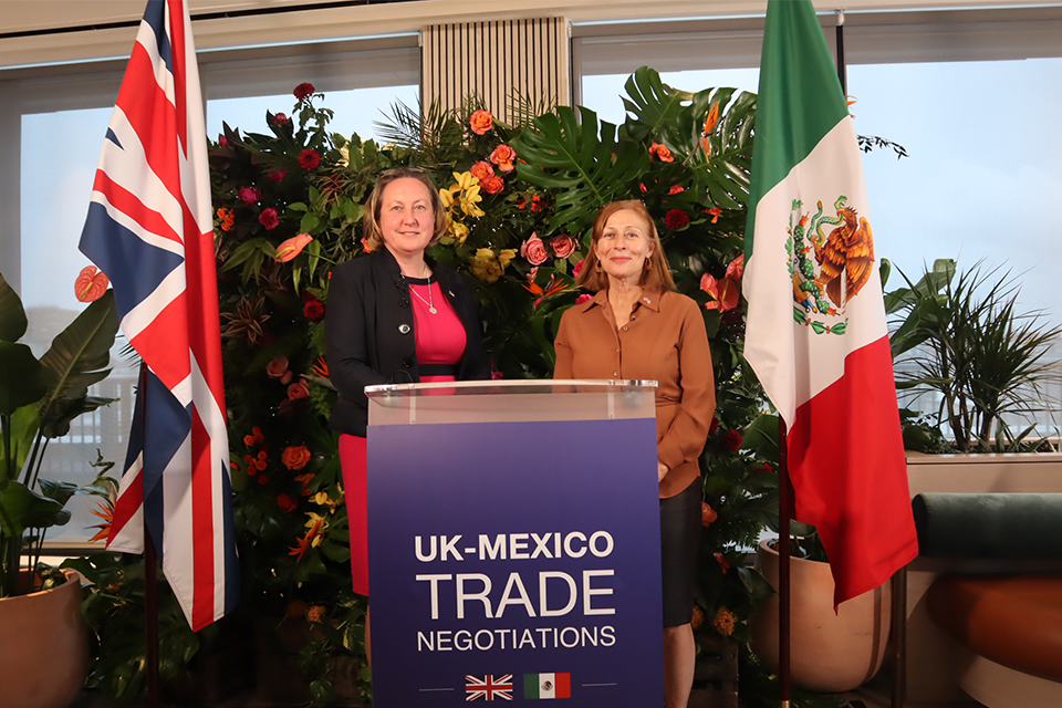 Anne-Marie Trevelyan and Tatiana Clouthier pose in front of a podium and the UK and Mexican flags.