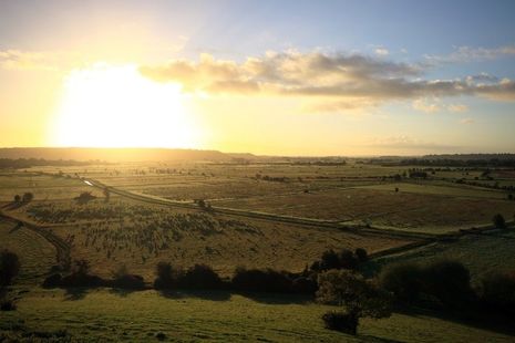 Image shows sunset over a patchwork of green fields.
