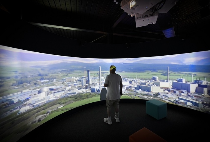 A man stood facing a large projector screen that features an aerial image of the Sellafield nuclear site