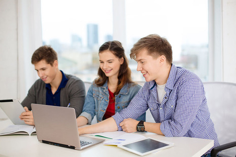 Three students around a laptop smiling.