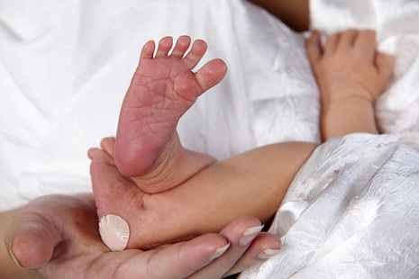 Baby held in mother's arms with plaster on one of baby's heels