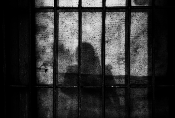 Shadow of prisoner standing behind bars.