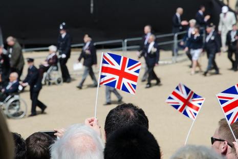 Британские флаги машут руками, а на заднем плане маршируют ветераны