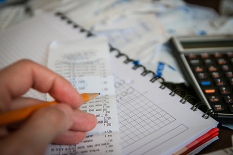 Hand holding pencil above desk paperwork and calculator