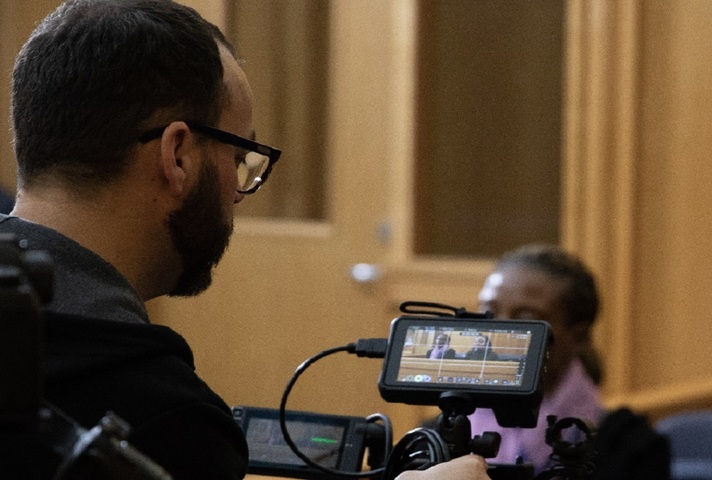 Video camera operator filming woman in court buildings.