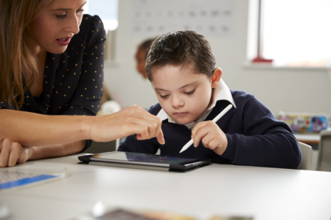 A child and a teacher working together on a tablet. 
