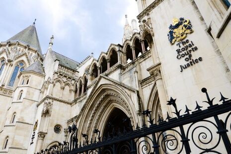 The exterior building of the Royal Courts of Justice in London. A grand building behind a black fence. 
