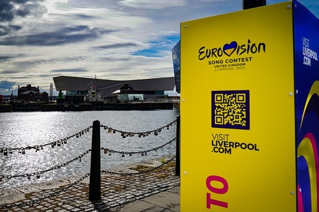 A view over Liverpool docks showing a Eurovision sign in the foreground and the arena where the contest is taking place across the water