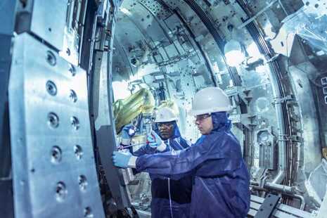 Two people wearing hard hats and protective clothing, operating a tool and torch, working inside a fusion energy machine training facility at UKAEA's Culham Campus