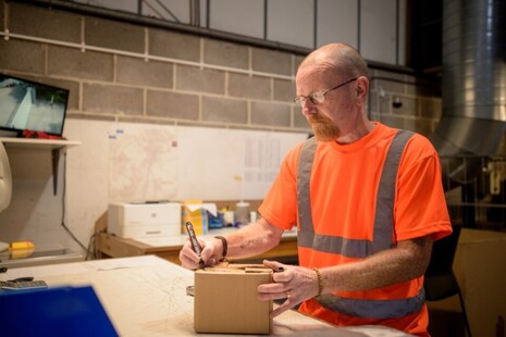 Person wearing a high-vis garment, using a marker to write on a cardboard box