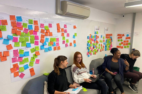 HMCTS User Research team seated in a room in front of a whiteboard with multicoloured post-it notes on