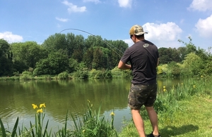 Man stands by lake fly fishing.