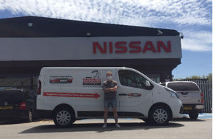 Images shows a man standing in front a Nissan van which is in front of a Nissan logo. The van has the logo for the Walking with the Wounded charity on it. The man has his arms crossed and is looking directly at the camera.