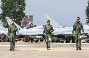 3 uniformed men walking in line in front of two Typhoon aircraft.