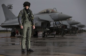 A pilot from 6 Squadron, RAF Lossiemouth, in front of a line of Typhoon aircraft in full flying attire.