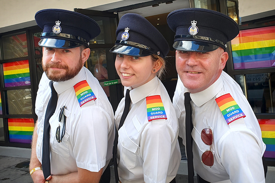 3 MOD-vakter bär epaulette med pride regnbågen på sin uniform. Det finns också Pride-flaggor på fönstren i bakgrunden.