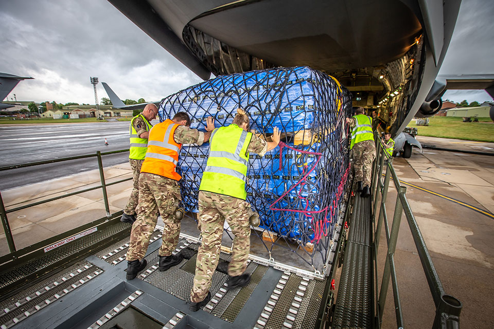 Image depicts three men loading a cargo pack into the back of a C-17 aircraft.