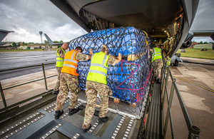 Image depicts three men loading a cargo pack into the back of a C-17 aircraft.
