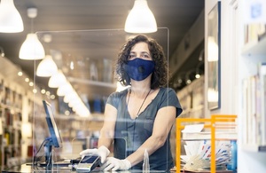 A woman behind the counter at a bookshop, wearing a face covering and protective gloves