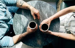 Man and woman holding cups on table.