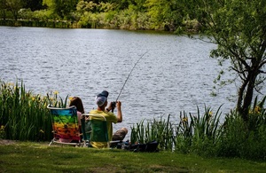 A man and woman sat fishing by a lake