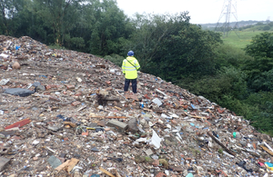 An Environment Agency officer in high viz stands on top of a large pile of mixed waste
