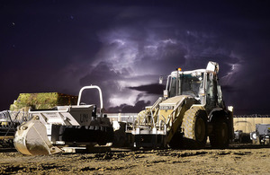 adepicts a mechanical vehicle on dirt ground with the background of lightning.