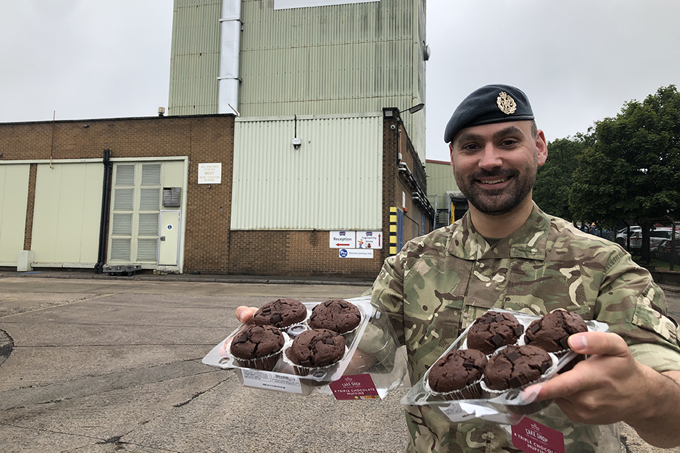 RAF Reservist Danny Railton holding trays of muffins and smiling at the camera.