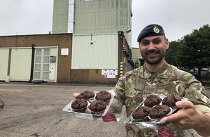 RAF Reservist Danny Railton smiling with two trays of muffins in his hands.