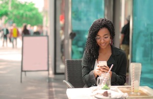 A smiling women on her phone sat outside a restaurant