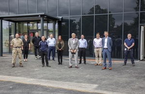 Project team, a mix of men and women, standing in front of new glass training facility smiling at the camera.