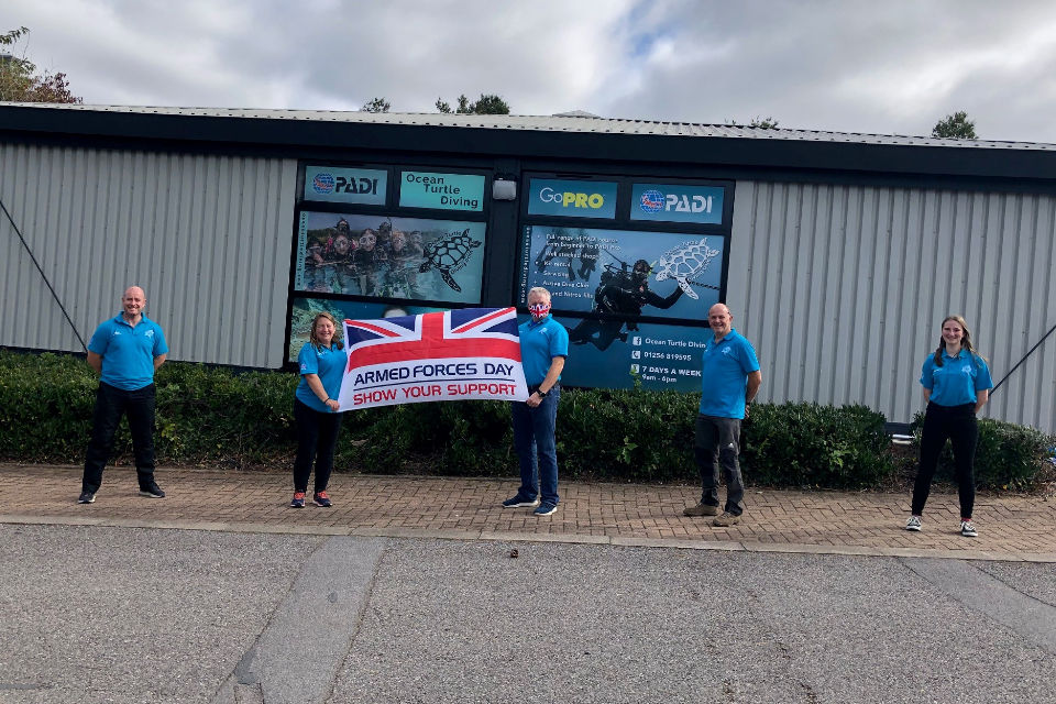 Members of staff from the Diving School standing outside and holding the Armed Forces Covenant flag.