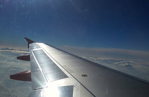 Shiny aeroplane wing above clouds viewed from inside plane.