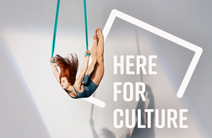 A circus acrobat performs in front of the Here for Culture logo