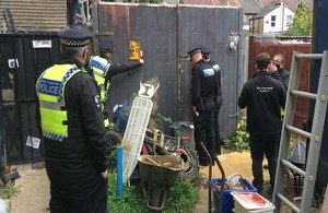 Image shows four police officers and two Environment Agency officers at the gates of a waste site. Around them are items of scrap metal