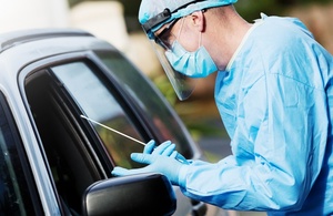 A man wearing personal protective equipment taking a swab though a car window