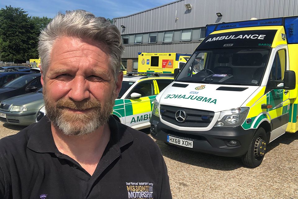 James Cameron standing in front of NHS ambulances smiling at the camera.