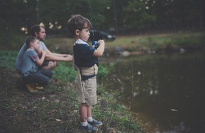 Young boy fishing with a younger boy and adult male fishing in the distance