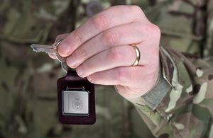 A member of the armed forces holding up a set of keys with the Ministry of Defence logo on a key ring.