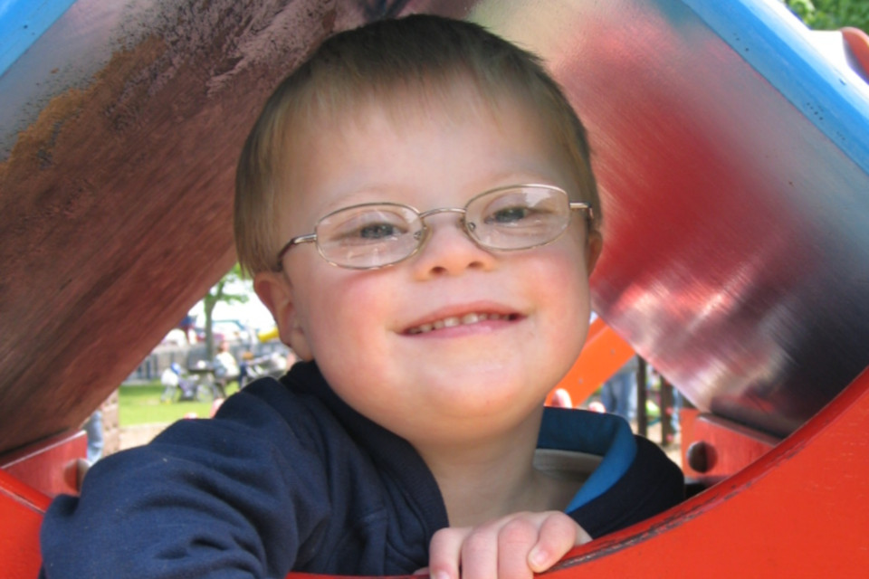 Um menino com síndrome de Down num parque infantil a olhar para a câmara
