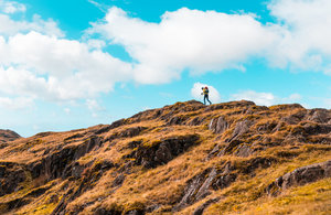 Image of man walking on rocks with blue sky behind